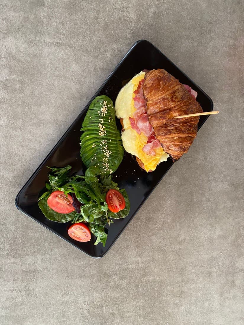 Croissant con jamón, huevo y palta sobre tabla negra
